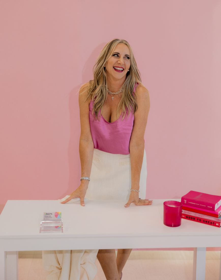 Stacey Berger smiling, leaning on a white desk against a pink wall
